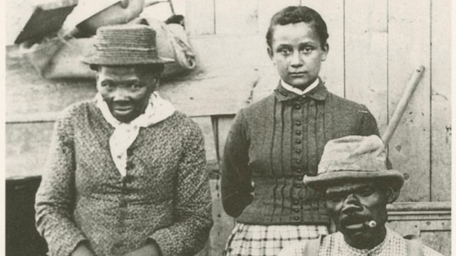 A group of three people; two women standing and a man seated.